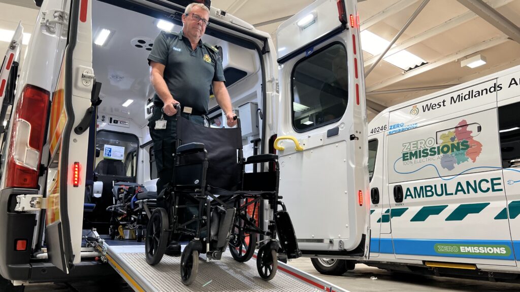 A photo of a man pushing an empty wheelchair down the ramp of a transport ambulance