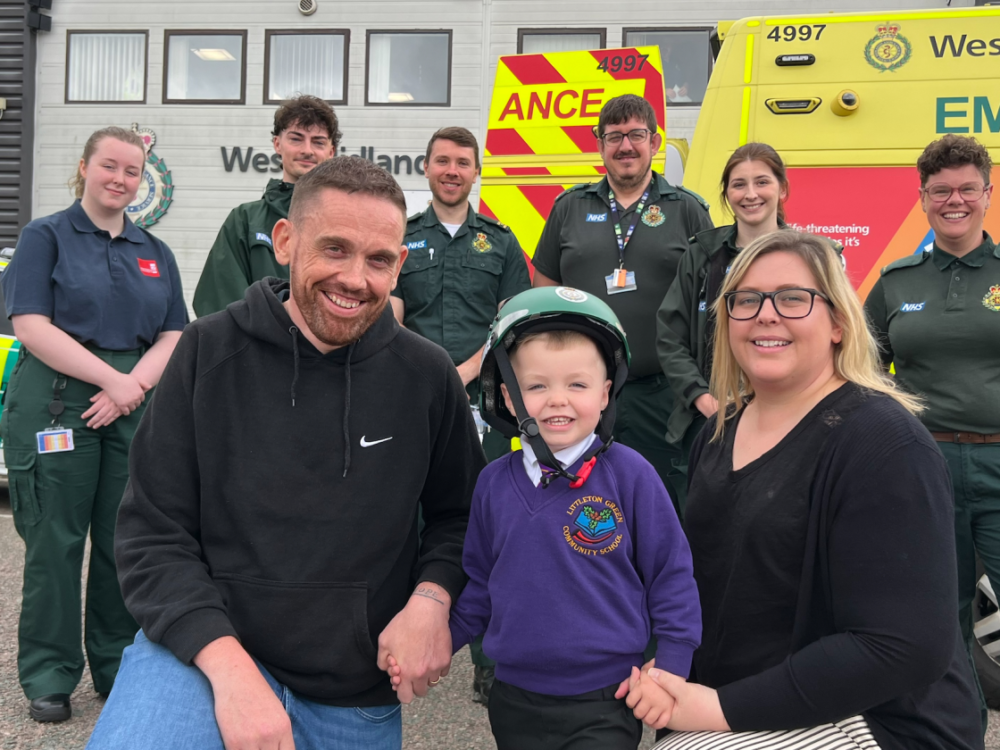 Ambulance staff standing behind a mum, dad and little boy outside infront of an ambulance.