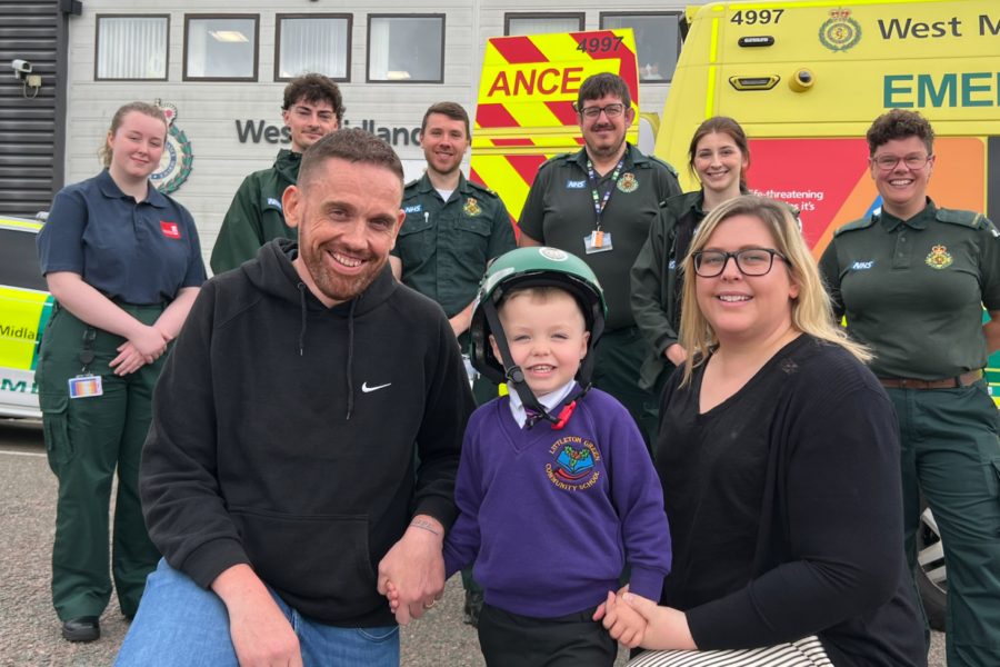 Ambulance staff standing behind a mum, dad and little boy outside infront of an ambulance.