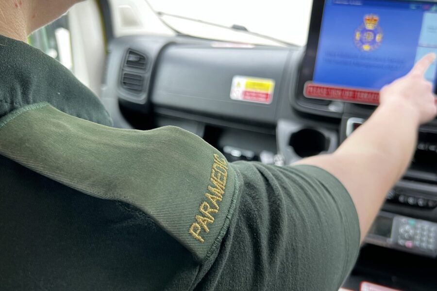 Paramedic pushing button on screen in front of ambulance cab whilst a passenger on a 999 call, photo over shoulder showing 'paramedic' epaulette.