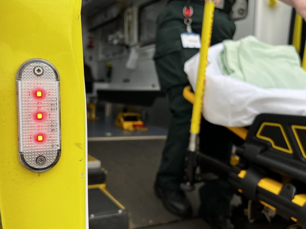 An ambulance crew member standing on ramp pulling stretcher up into ambulance.