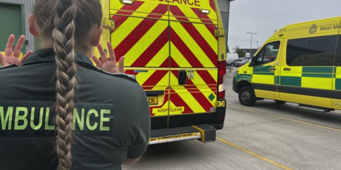 Ambulance technician at stoke waving hands standing behind reversing ambulance being banksman to help vehicle park