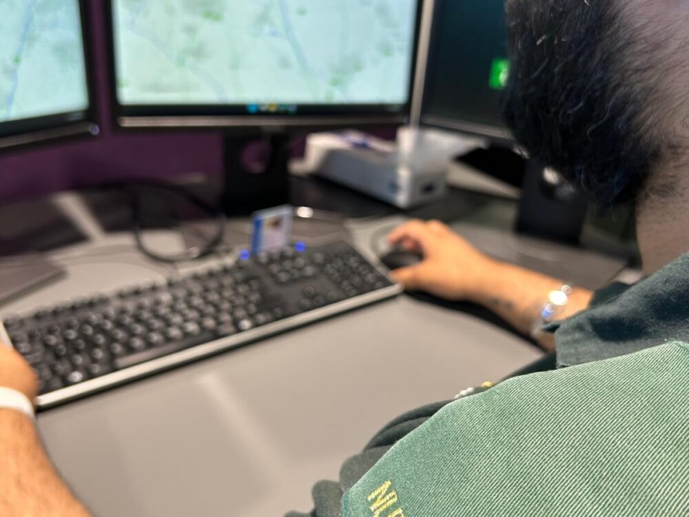 Image of man sitting in front of 999 control room computer screen with green uniform on and 'nurse' epaulettes on shoulder. Photo shows epaulette of nurse in green uniform.