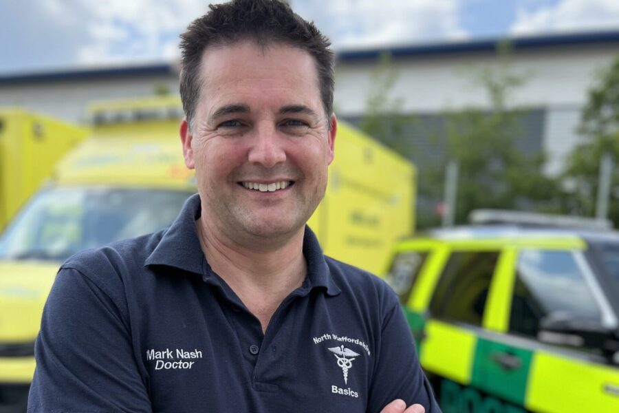 North Staffs BASICS doctor smiling at camera with doctor response car and ambulance major incident vehicle in background