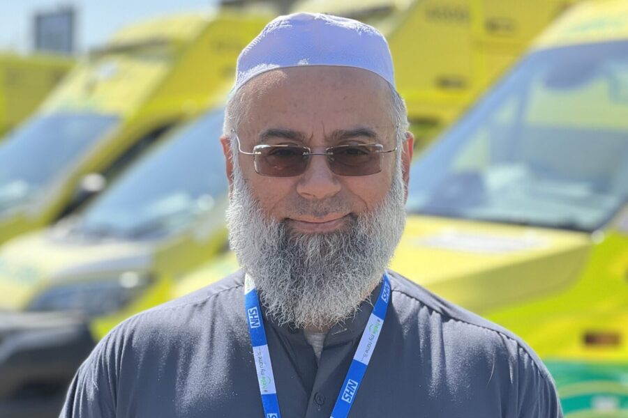 Trust Muslim Chaplain Imam Mohammad Asad smiling at camera with a row of ambulances in background