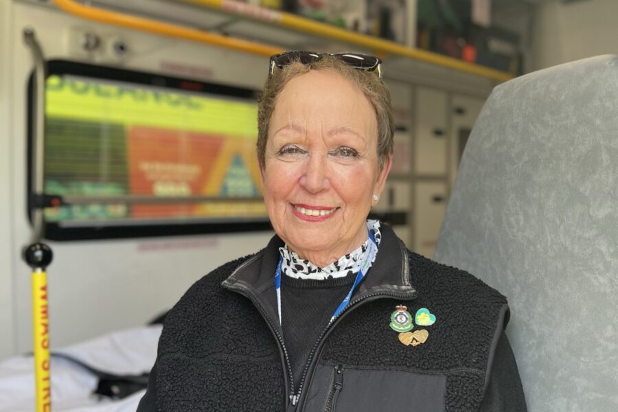 Public Governor for Staffordshire Eileen Cox smiling at camera whilst sitting in back of ambulance with stretcher in background.