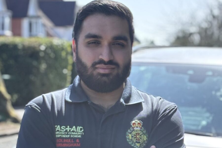 CFR Hiran Patel wearing blue uniform looking at camera with arms folded standing infront of bonnet of community response car