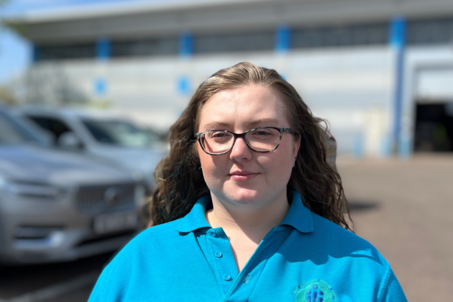 Staff Advice Liaison Service advisor Abigail Smith wearing blue SALS uniform smiling at camera with cars and building in background