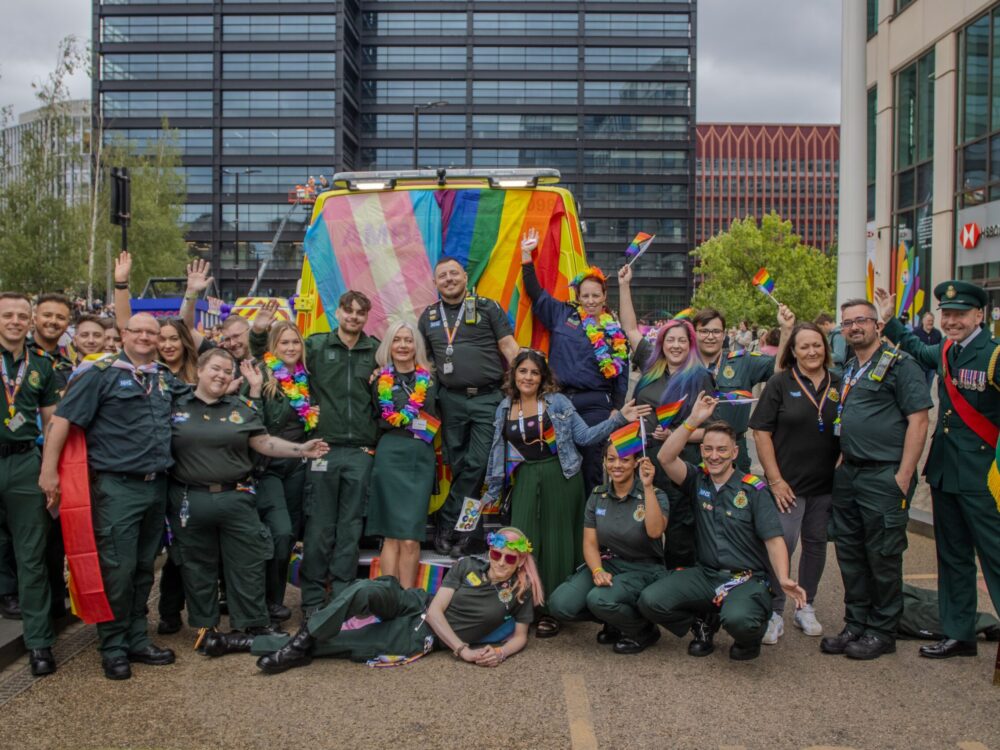 A group of staff pose behind an Incident Support Unit covered in LGBTQ+ and Trans flags at Birmingham Pride Parade