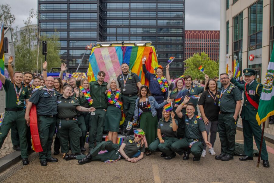 A group of staff pose behind an Incident Support Unit covered in LGBTQ+ and Trans flags at Birmingham Pride Parade