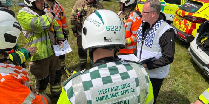 Group of emergency service staff from fire, police and ambulance wearing full uniform and helmets in a circle talking with each other at an incident