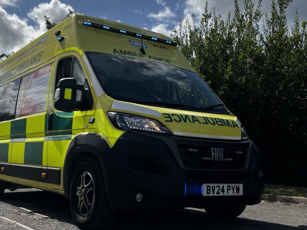 Ambulance driving past camera under a cloudy sky