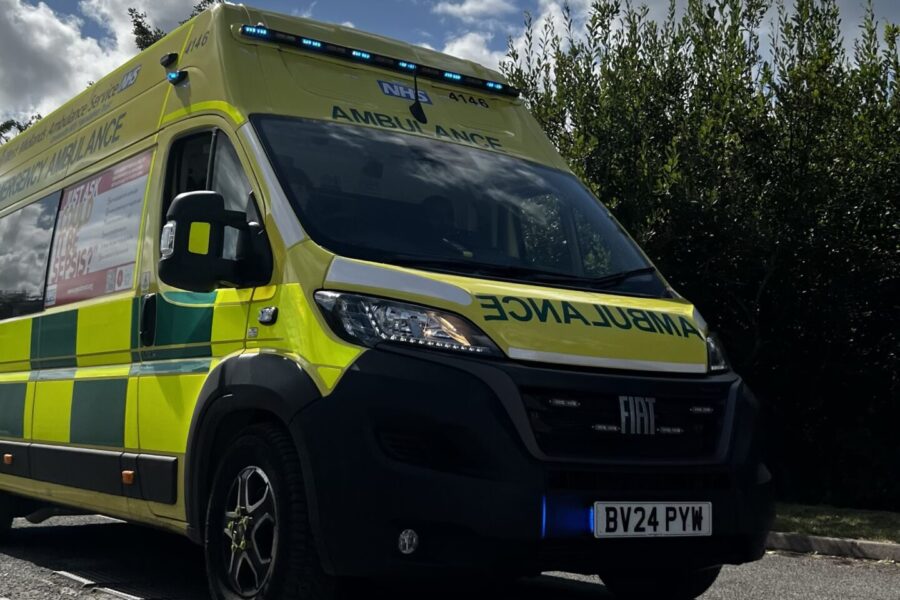 Ambulance driving past camera under a cloudy sky