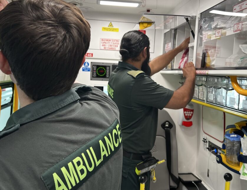 Ambulance crew with backs to camera reaching into cupboards to get equipment