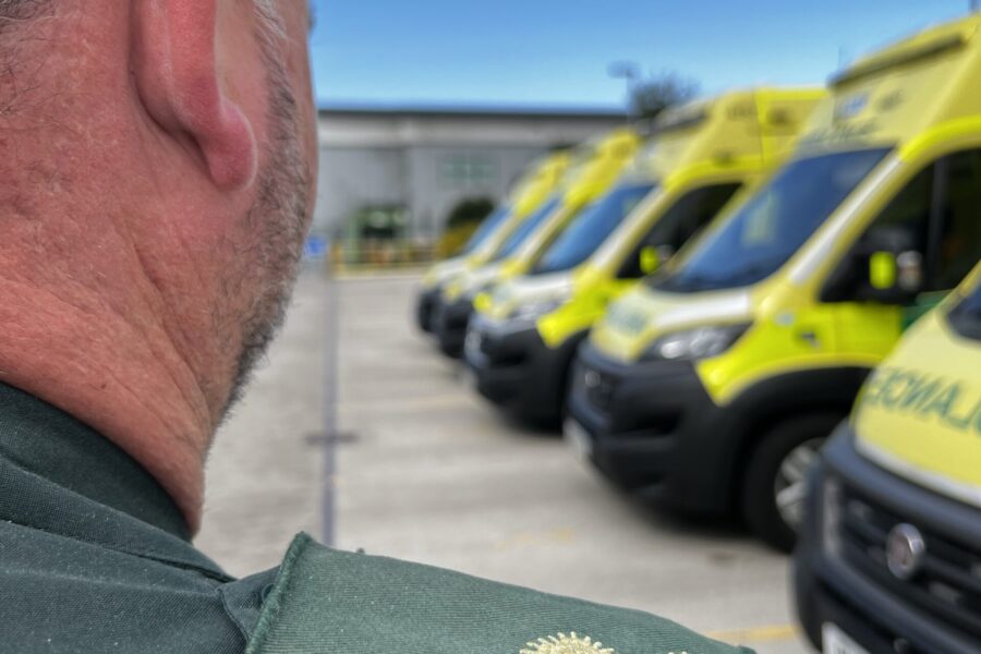 Paramedic officer with two pip epaulettes on shoulder facing away from camera looking at row of ambulances parked up.