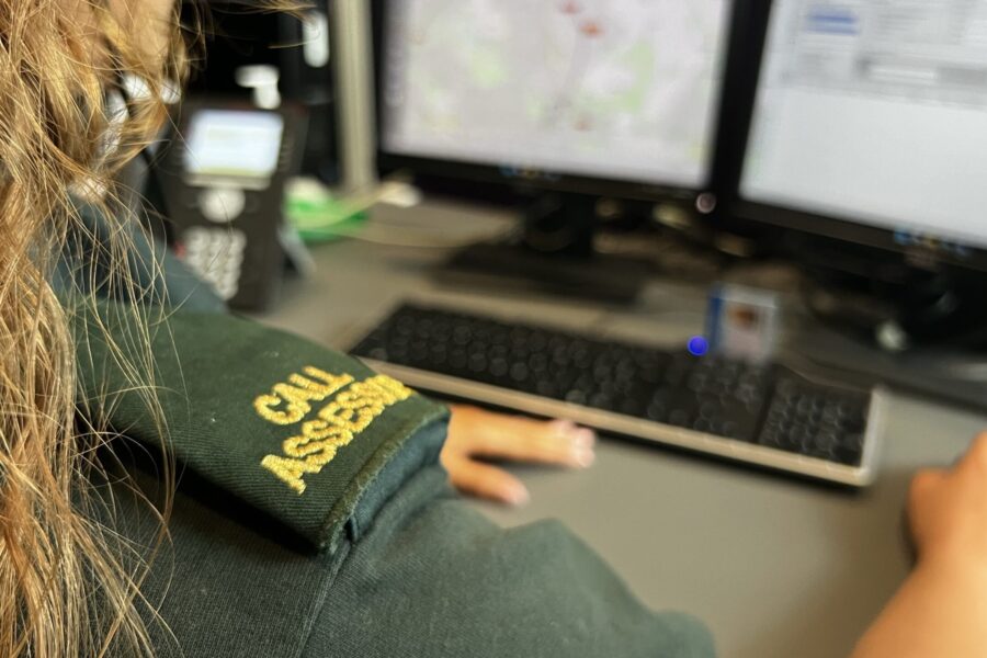 Female 999 call assessor sitting at computer with call assessor epaulettes on shoulder