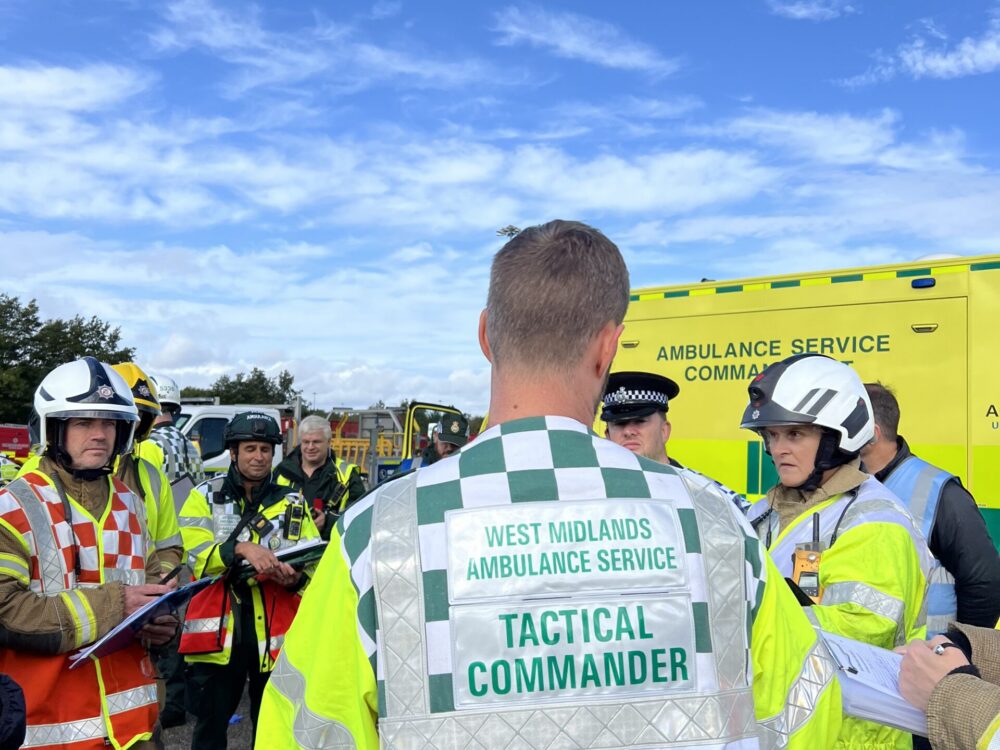 JESIP meeting at scene of major incident exercise with ambulance, police, fire and other agencies wearing high viz and helmets