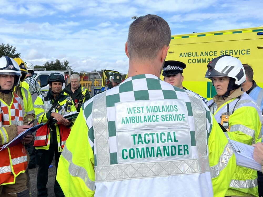 JESIP meeting at scene of major incident exercise with ambulance, police, fire and other agencies wearing high viz and helmets