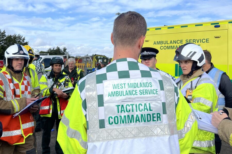 JESIP meeting at scene of major incident exercise with ambulance, police, fire and other agencies wearing high viz and helmets