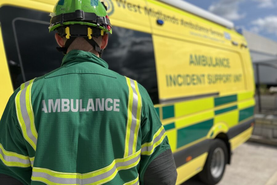 HART paramedic in green overalls and helmet standing with back to camera. HART Ambulance in background.